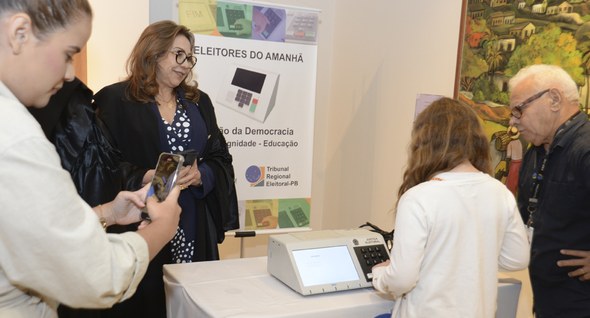 #PraTodosVerem: Na fotografia aparece crianças em uma fila, ao fundo uma mesa com uma urna eletr...