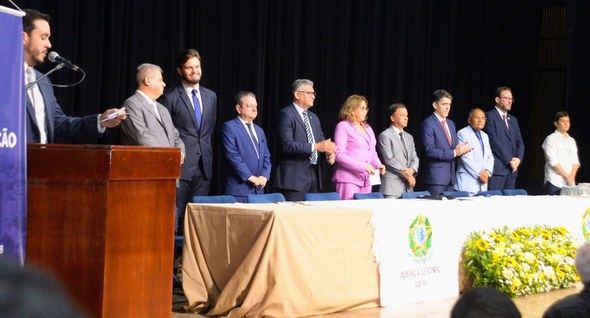 #PraTodosVerem: Em um palco com fundo preto, um grupo de nove pessoas, vestidas formalmente, est...