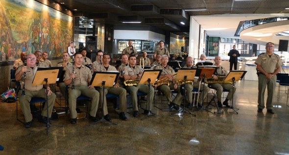 #PraTodosVerem: Um grupo de músicos militares em uniformes bege está sentado com instrumentos de...