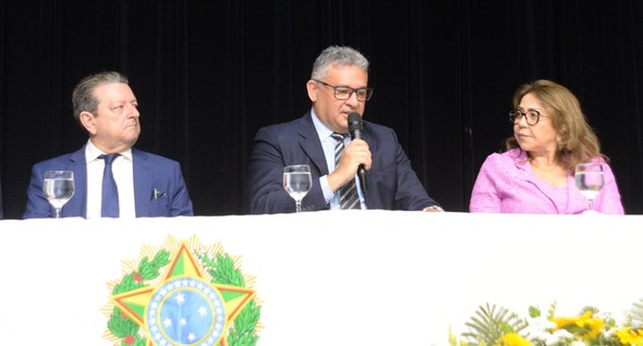 #PraTodosVerem: Na fotografia aparecem dois homens e uma mulher, em uma mesa de honra, um dos ho...