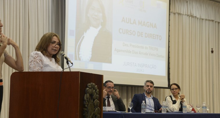 Painel retangular com uma mulher falando ao publico.