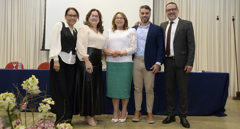 Painel retangular com cinco pessoas de pé, dois homens e três mulheres.