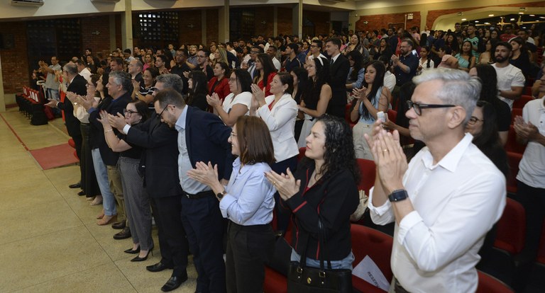 Painel retangular pessoas num auditório aplaudem de pé.