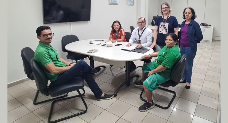 #ParaTodosVerem: Painel retangular com pessoas reunidas em volta de uma mesa, quatro sentadas e ...