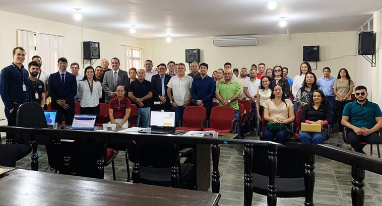 Painel retangular com pessoas de pé e sentadas, posando para fotografia, numa sala de julgamentos.