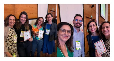 #PraTodosVerem: Na fotografia aparecem duas mulheres, em pé, posando, com o banner do 4º FestLab...