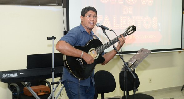 #PraTodosVerem: Na fotografia aparece um homem cantando em um microfone e tocando violão.