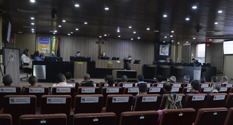 Painel retangular com pessoas num tribunal em reunião.