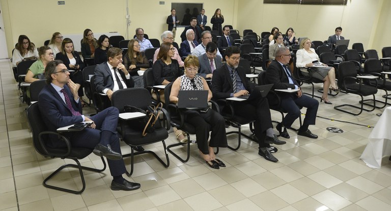 Painel retangular com pessoas sentadas, participando de reunião de trabalho.