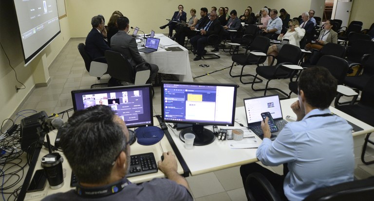 Painel retangular com pessoas em volta de uma mesa, em reunião de trabalho.