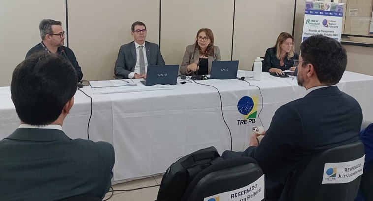 Painel retangular com pessoas em volta de uma mesa, em reunião de trabalho.